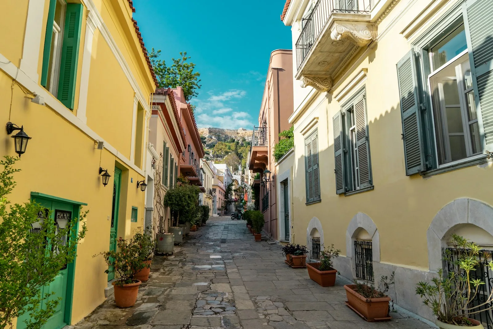 Callejón peatonal empedrado con tabernas y plantas en el histórico barrio de Plaka
