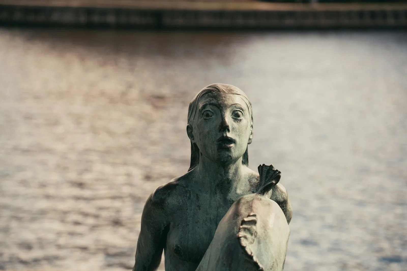 Estatua de bronce de La Sirenita posada sobre una roca junto a la bahía del puerto de Copenhague