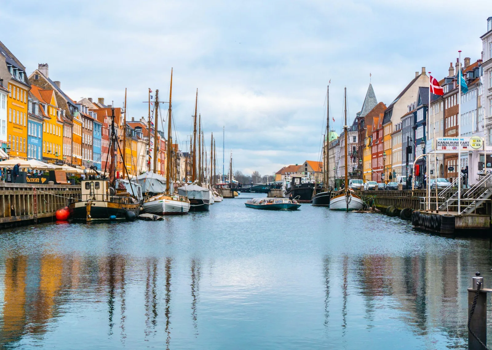 Paseo adoquinado de Nyhavn con terrazas al aire libre y mástiles de veleros tradicionales