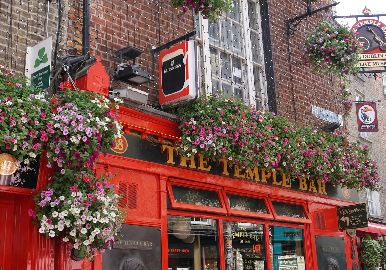 Fachada roja tradicional del pub The Temple Bar adornada con flores y faroles en una calle empedrada