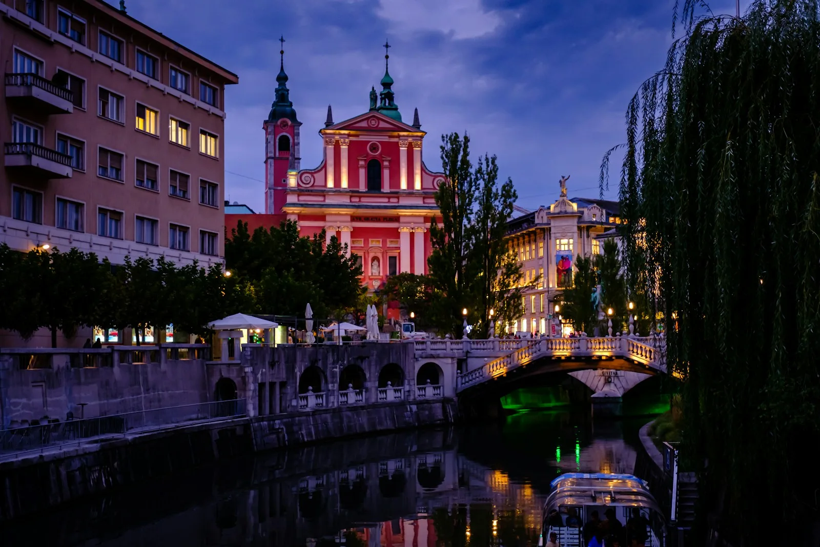 Río Ljubljanica con sus sauces llorones, terrazas animadas y el Castillo medieval en la colina al atardecer
