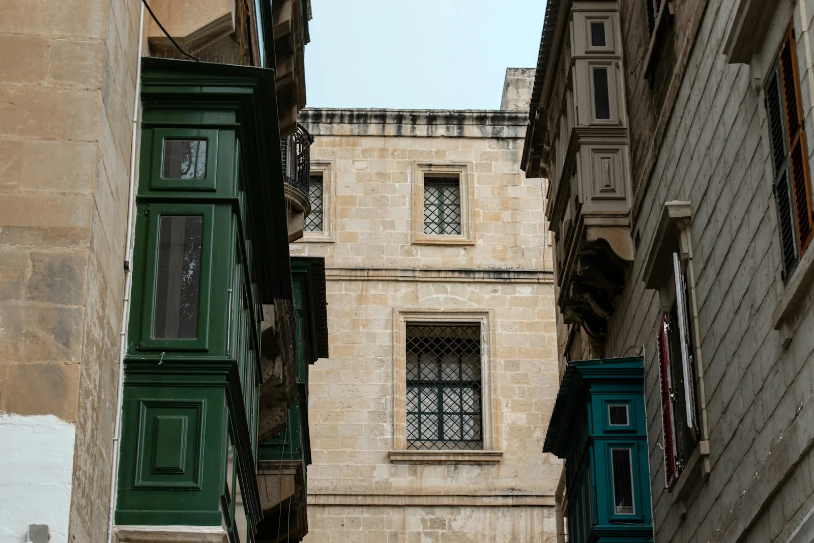 Calle empinada de piedra caliza dorada con tradicionales balcones de madera en La Valeta